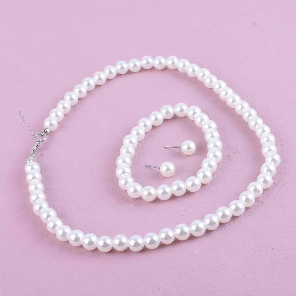Pearl necklace, bracelet and stud earrings set on a pink backdrop
